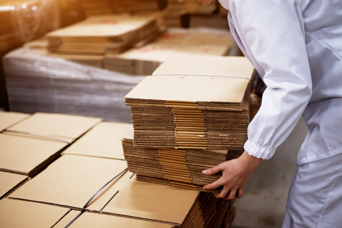 Close Up Of Young Female Worker Picking Up Stacks Of Folded Card